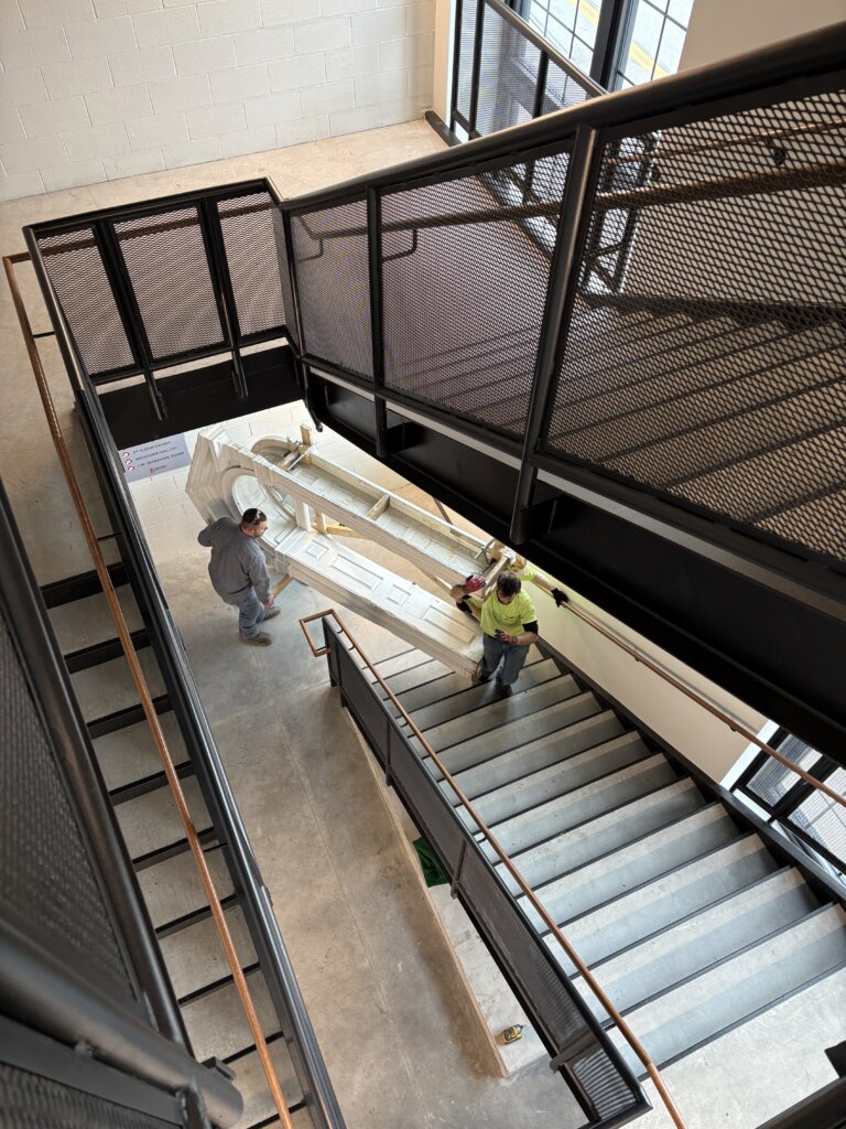photo of workers carrying a large wooden door up a flight of stairs