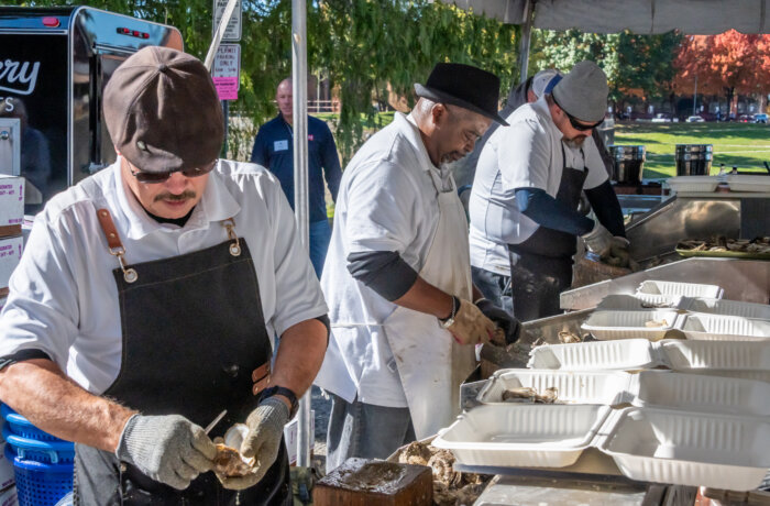 a row of three oyster shuckers wearing aprons and gloves