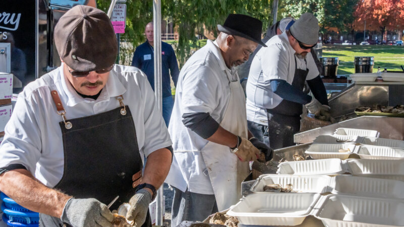 a row of three oyster shuckers wearing aprons and gloves