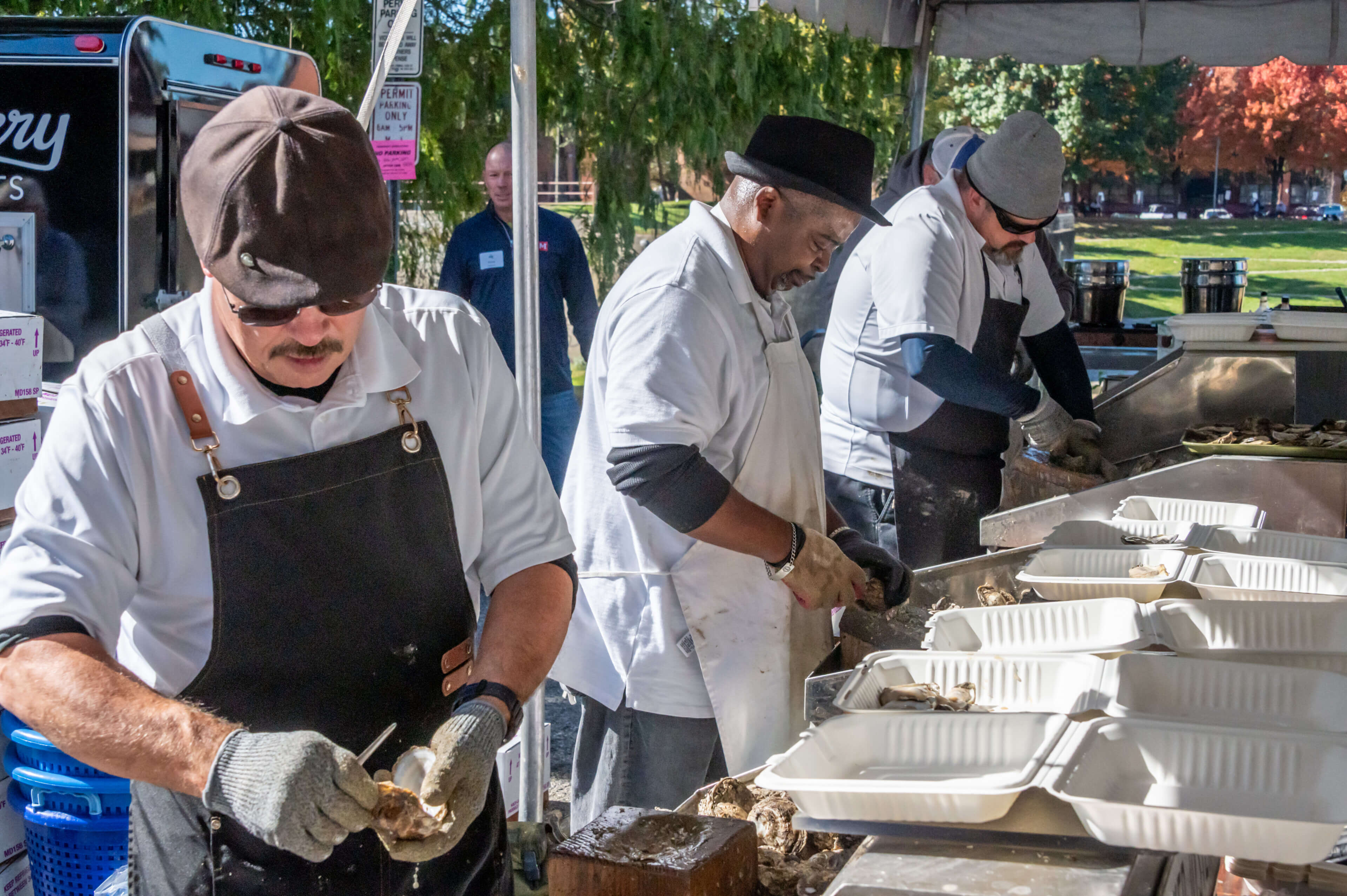 a row of three oyster shuckers wearing aprons and gloves