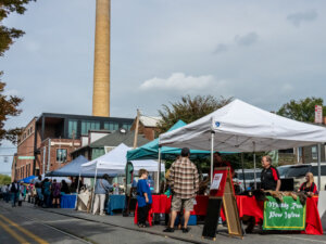 people browsing at tents along Pershing Avenue with the History Center smokestack in the background